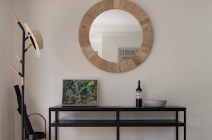 A round mirror on a wall, a black console table with a framed painting and a bottle, and a floor lamp with a wooden base. - Private Creek | Executive Home | Kayaks & Zipline (Sunshine Coast)