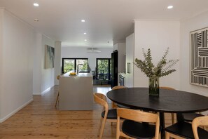 A modern interior with a dining area, a kitchen, and a view of the outdoors. - Private Creek | Executive Home | Kayaks & Zipline (Sunshine Coast)