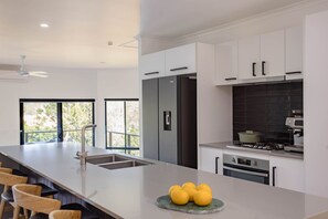 Une cuisine moderne dotée d’un îlot central, d’appareils électroménagers en acier inoxydable et offrant une vue sur l’extérieur.
