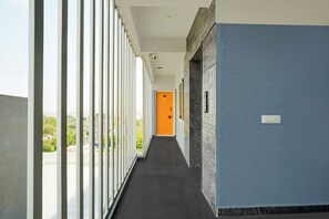 A corridor with a view of greenery outside, a door with a number sign, and a security camera on the ceiling. - Super Hotel O Acharya Institute Of (Bengaluru)