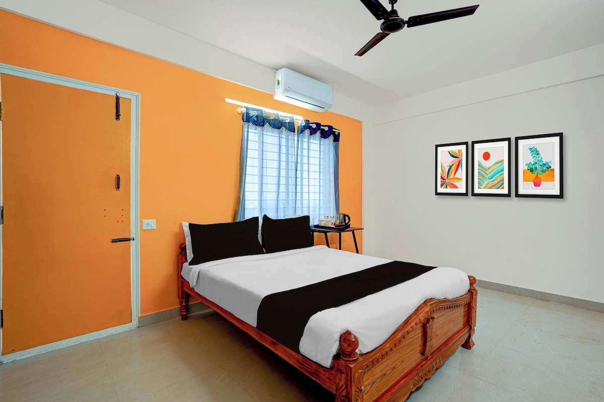 A bedroom with a bed, a ceiling fan, an air conditioning unit, a window with curtains, and three framed artworks on the wall.
