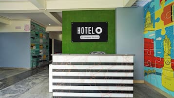 Una recepción de hotel con un cartel que dice 'HOTEL' arriba, una pared verde y un mural colorido a la derecha.