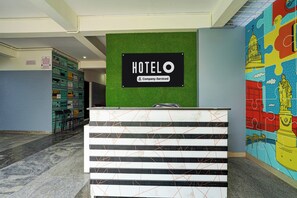 A hotel reception desk with a 'HOTEL' sign above it, a green wall, and a colorful mural on the right.