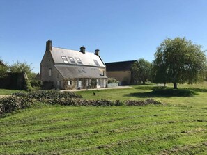A large stone house with a sloped roof and multiple chimneys, surrounded by a well-maintained lawn and a tree. - New Listing (La Cambe)