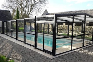 A swimming pool with a glass enclosure and a stone wall in the background. - New Listing (La Cambe)