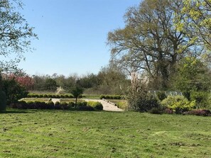 A well-maintained grassy area with a variety of trees and shrubs, a clear sky, and a pathway leading through the landscape. - New Listing (La Cambe)