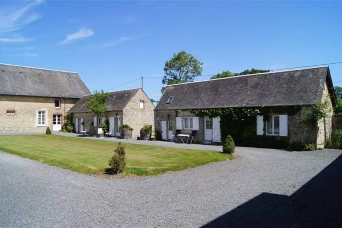 A row of stone buildings with a gravel driveway and a small lawn.