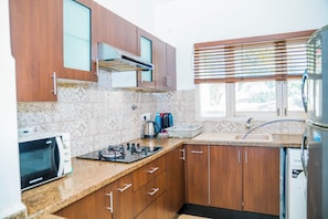 A kitchen with wooden cabinets, a gas stove, a microwave, and a refrigerator. - Charming 3-bedroom apartment with AC in peaceful Candolim (Arpora)