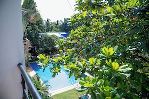A swimming pool surrounded by lush greenery, with a clear view of the sky and a building in the background. - Charming 3-bedroom apartment with AC in peaceful Candolim (Arpora)