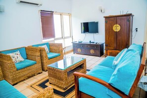 A living room with wicker furniture, a flat-screen TV, and a wooden cabinet. - Charming 3-bedroom apartment with AC in peaceful Candolim (Arpora)
