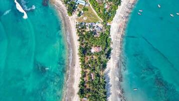 An aerial view of a coastal property with a beachfront, a central road, and scattered buildings.