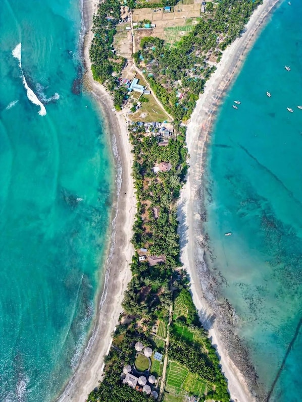 An aerial view of a coastal property with a beachfront, a central road, and scattered buildings.