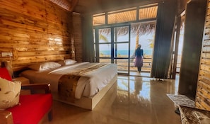 A wooden cabin room with a bed, a red chair, and a view of the beach. - LuiPaz Resort Saintmartin (Saint Martin's Island)