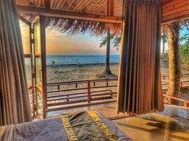 Quarto com vista para a praia, deck de madeira e telhado de palha.