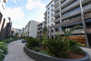 A modern multi-story residential building with balconies, a landscaped courtyard with tropical plants, and a clear sky. - Spacious Seaviews (Melbourne)
