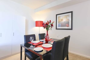 A dining area with a table set for four, a red vase with flowers, a framed picture on the wall, and a white wardrobe. - Spacious Seaviews (Melbourne)
