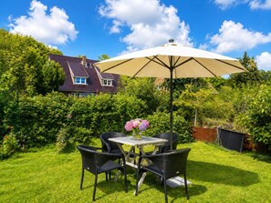 A patio with a table and chairs, a large umbrella, and a house in the background. - Beach Blossom in Margarethenhof (Wyk auf Foehr)