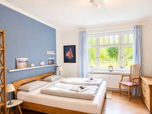 A hotel room with a double bed, a chair, a desk, and a window with a view of greenery. - Beach Blossom in Margarethenhof (Wyk auf Foehr)