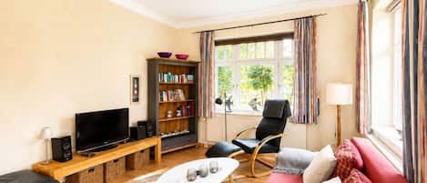 Una sala de estar moderna con un televisor de pantalla plana, una estantería, un sofá y una ventana con cortinas.