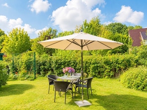 An outdoor dining area with a table and chairs, a large umbrella, and a vase of flowers. - Beach Blossom in Margarethenhof (Wyk auf Foehr)