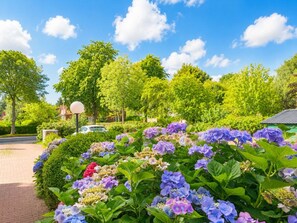Ein Garten mit verschiedenen Hortensienblüten, einem gepflasterten Weg und einem Gebäude mit Gründach im Hintergrund.