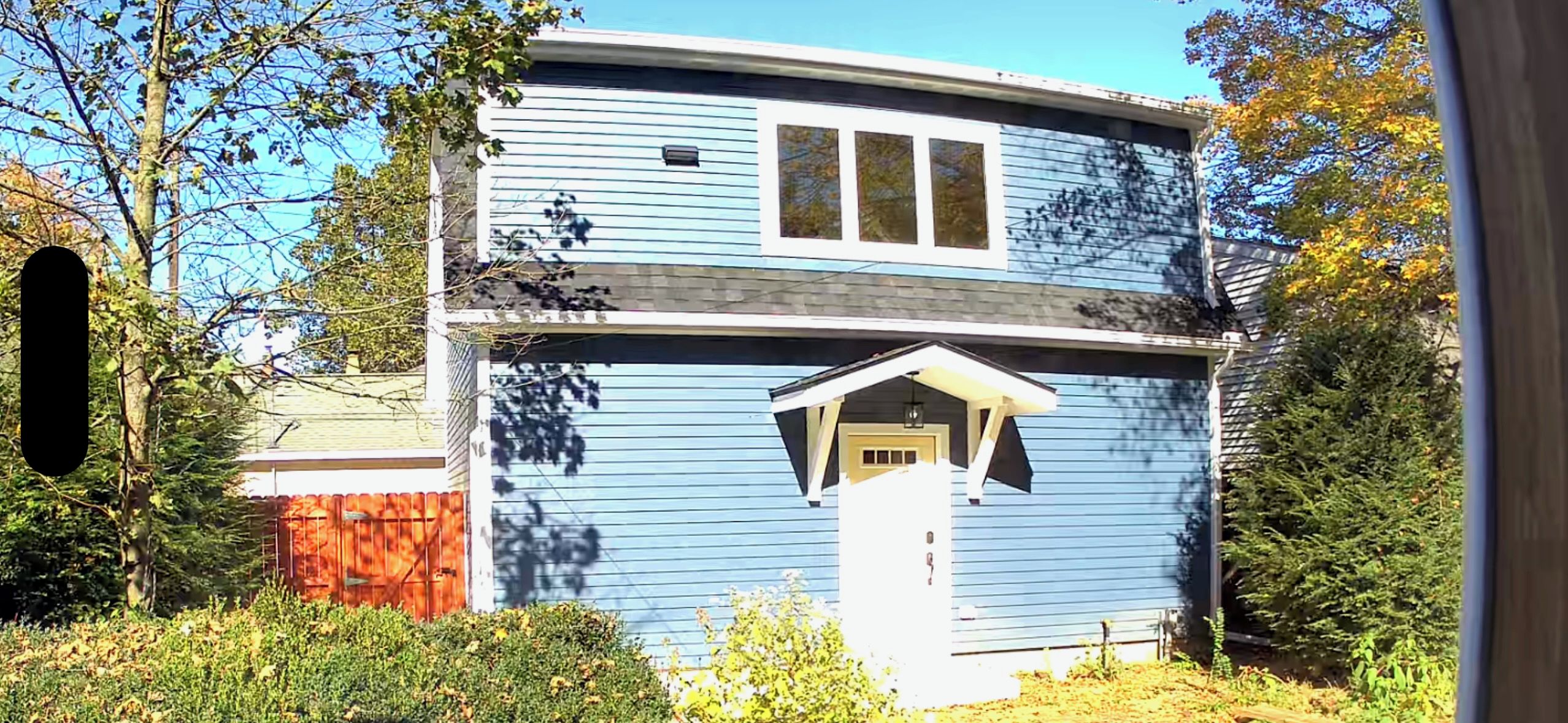 Ein zweistöckiges Haus mit Veranda und einem kleinen Anbau für eine Garage.