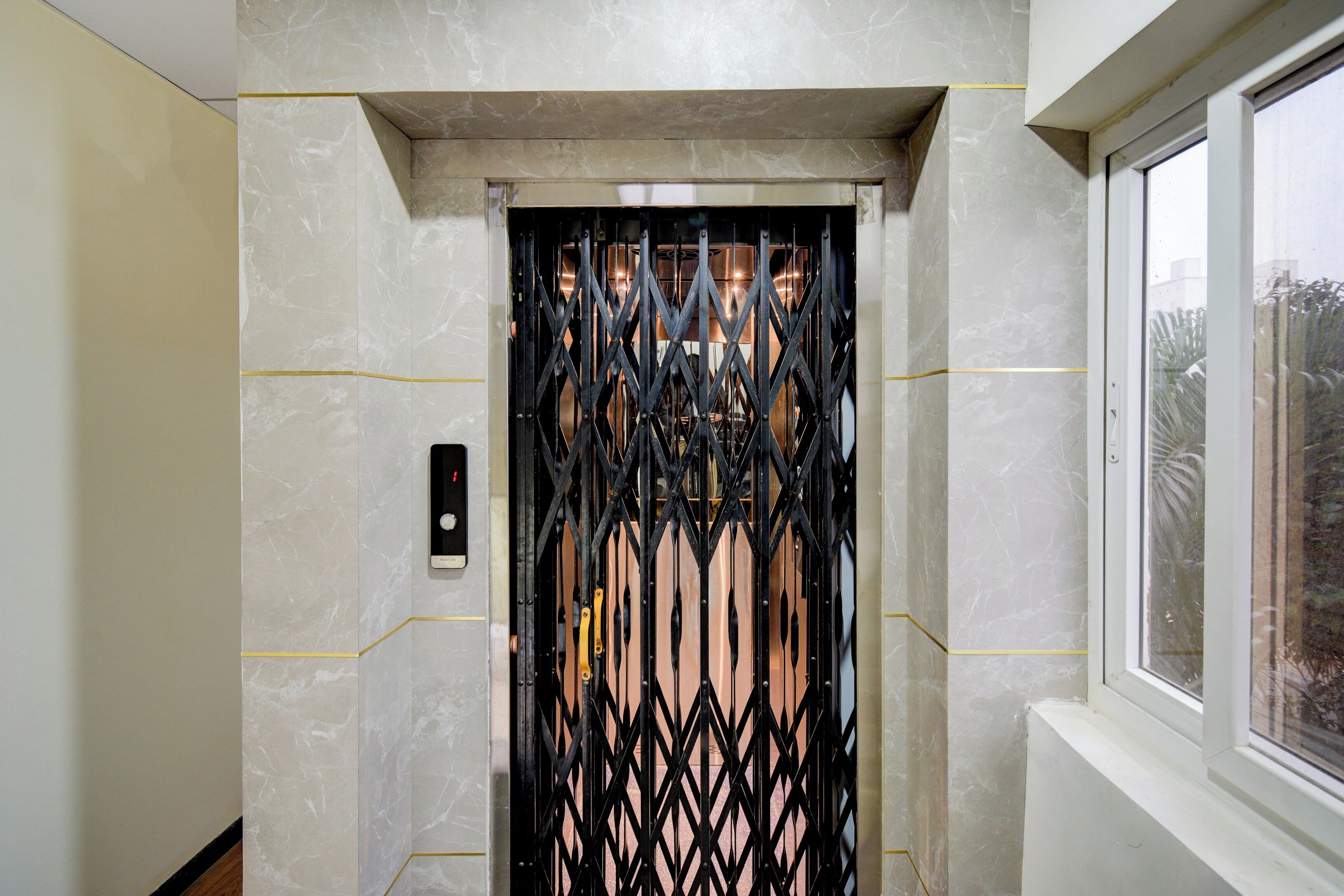 Un ascensor con una puerta metálica, un panel de control y una ventana a la derecha.