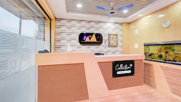 A reception desk with a logo, a ceiling fan, a wall-mounted clock, and a decorative fish tank.