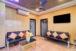 A reception area with two black leather sofas, a glass coffee table with a vase of flowers, a ceiling fan, and a mounted flat-screen TV. - Super Collection O Kollur Prime Arena (Hyderabad)