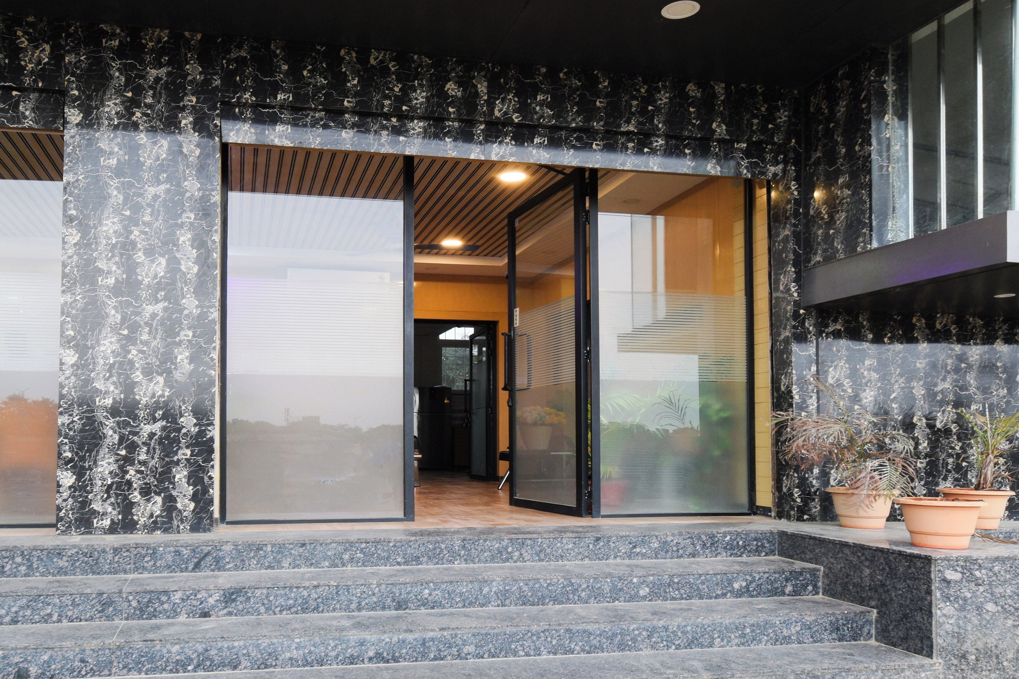 A building entrance with a glass door, steps leading up to it, and potted plants on the right.