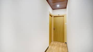 A narrow hallway with a wooden door at the end, a ceiling with a slatted design, and a light fixture.