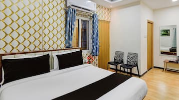 A hotel room with a bed, a window with curtains, a wall-mounted air conditioner, and a small table with a kettle.