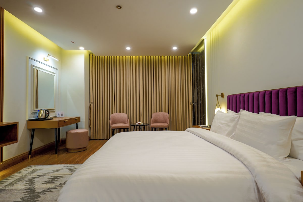 A hotel room with a large bed, two chairs, a desk with a mirror, and a nightstand.