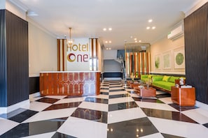 A hotel lobby with a check-in counter, a reception desk, a staircase, and a seating area with a sofa and coffee table. - Hotel One Top City Islamabd  (Islamabad)