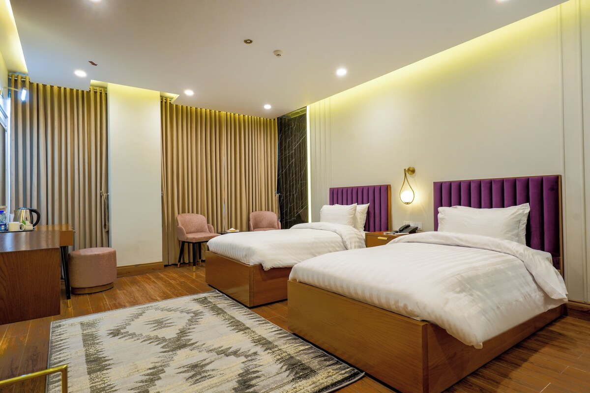 A modern hotel room with two beds, a desk, a chair, and a patterned rug.
