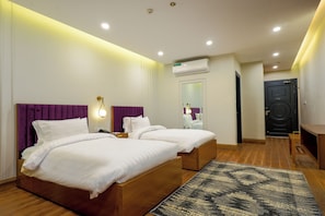 A hotel room with two beds, a wooden floor, a patterned rug, a wall-mounted air conditioner, and a door with a modern design. - Hotel One Top City Islamabd  (Islamabad)
