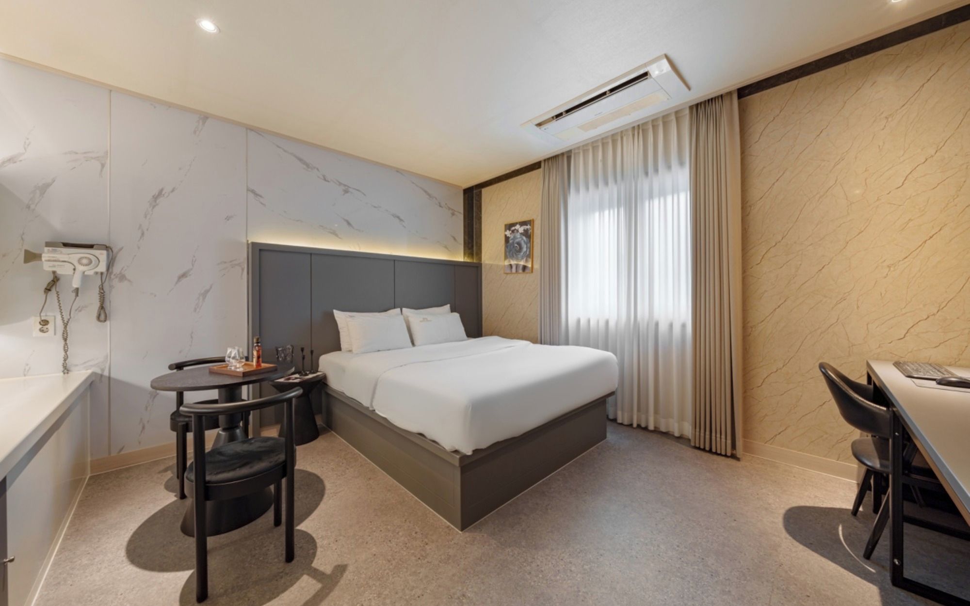 A hotel room with a bed, bedside table, chair, and a desk with a chair.