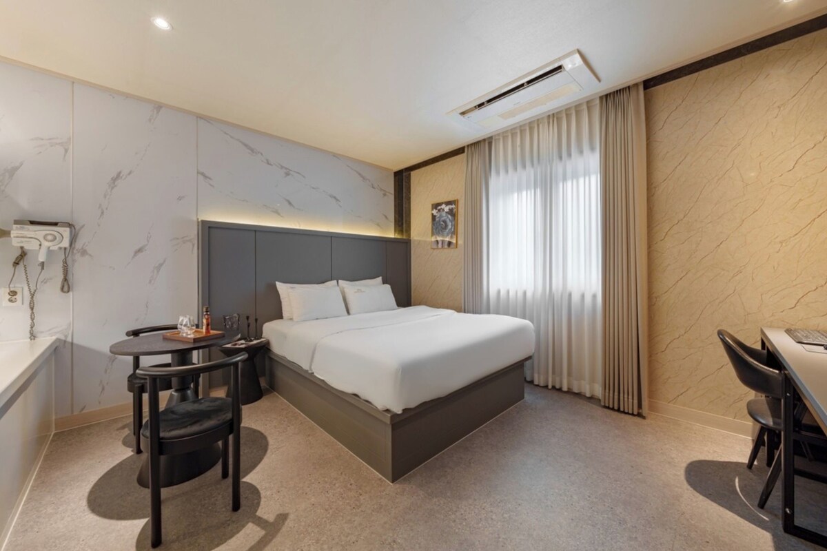 Una habitación de hotel con cama, mesita de noche, silla y escritorio con otra silla.
