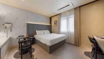 A hotel room with a bed, bedside table, chair, and a desk with a chair.