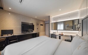 Habitació d'hotel amb llit, escriptori amb ordinador, televisió, bany amb mirall i taula petita amb safata.