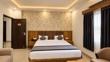Habitación de hotel con una cama grande, cabecera de madera, mesita de noche, escritorio, sofá y ventilador de techo.