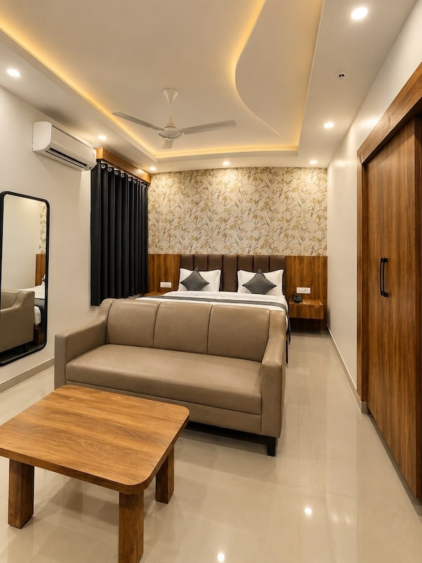A modern hotel room with a sofa, a wooden table, a ceiling fan, and a bed with a headboard. - Eastwyn Stays (Lucknow)