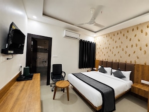 A hotel room with a bed, a desk, a chair, a television, an air conditioning unit, and a ceiling fan. - Eastwyn Stays (Lucknow)