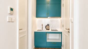 A narrow hallway with wooden flooring, white walls, and teal cabinets with gold handles.