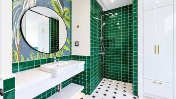A bathroom with a white sink, a mirror, green tiles, a shower, and a white cabinet.