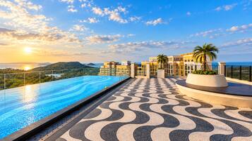 A rooftop infinity pool with a patterned floor, overlooking a coastal landscape with buildings and palm trees.