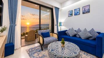 A modern living room with a blue sofa, patterned rug, and a view of the sunset through a glass door.