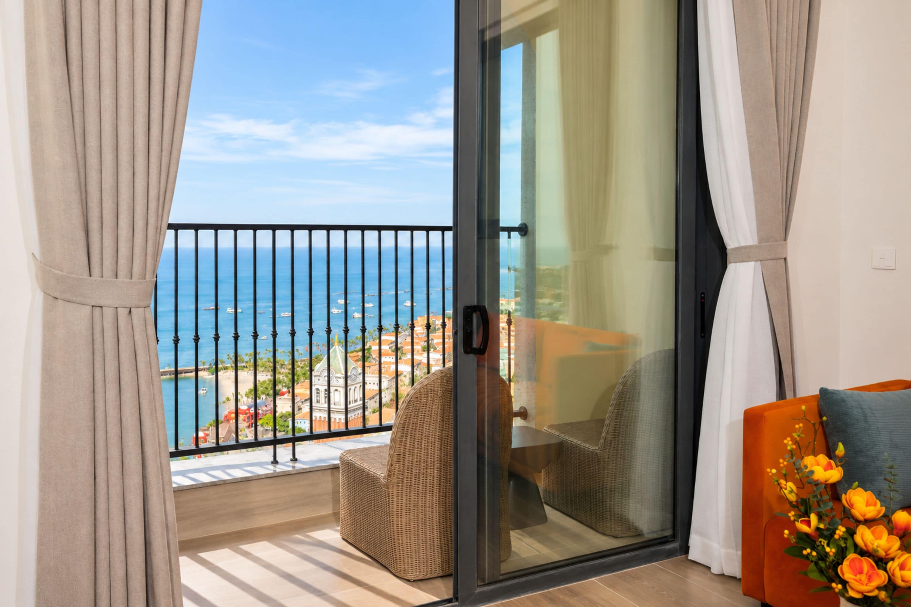 A balcony with a view of the sea, a wicker chair, and a sofa with a vase of flowers.