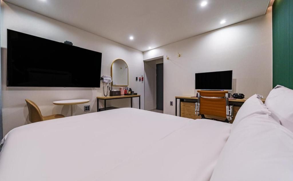 A hotel room with a large bed, a desk, a chair, a small table, a mirror, and a television.