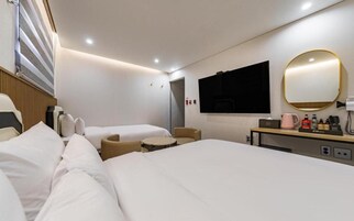 Habitación de hotel con dos camas, un sofá, una mesita, un televisor, un espejo y un minibar.